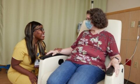 Nurse speaking with a masked patient seated in an infusion chair