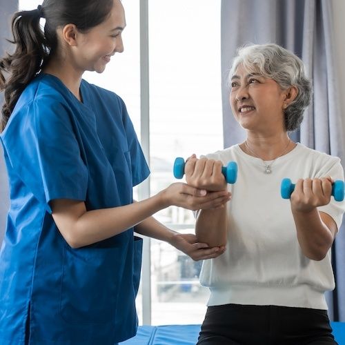 Physical therapist assisting an older woman with dumbbell exercises