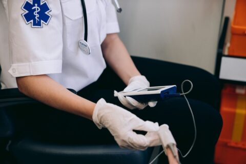 Gloved healthcare worker using a handheld monitor to check vital signs